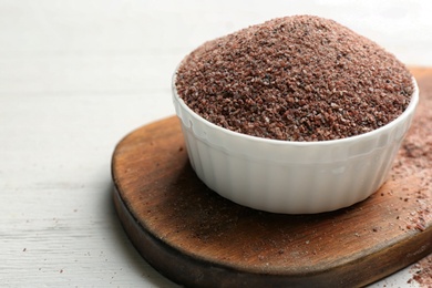 Photo of Black salt in bowl on white wooden table. Space for text