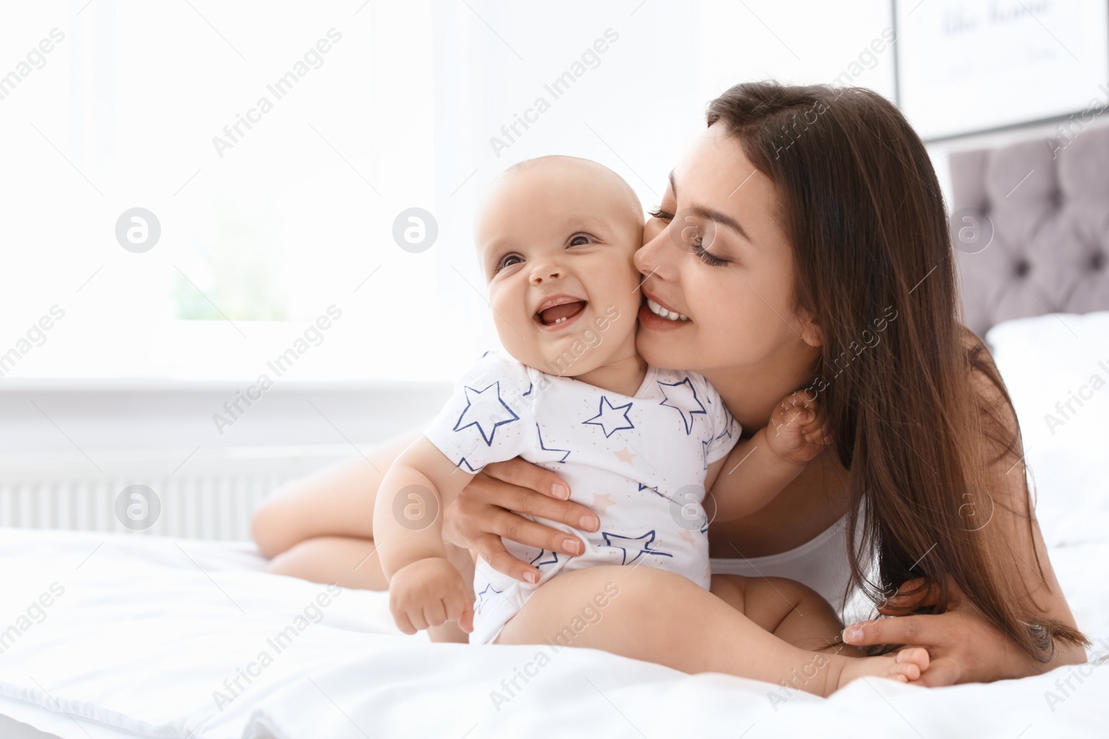 Photo of Young mother with her cute baby girl on bed at home