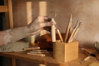 Photo of Clay crafting tools. Woman with wooden loop holder in workshop, closeup