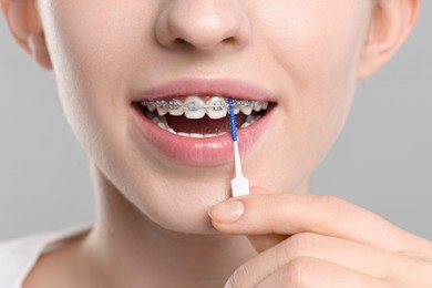 Photo of Woman with dental braces cleaning teeth using interdental brush on grey background, closeup