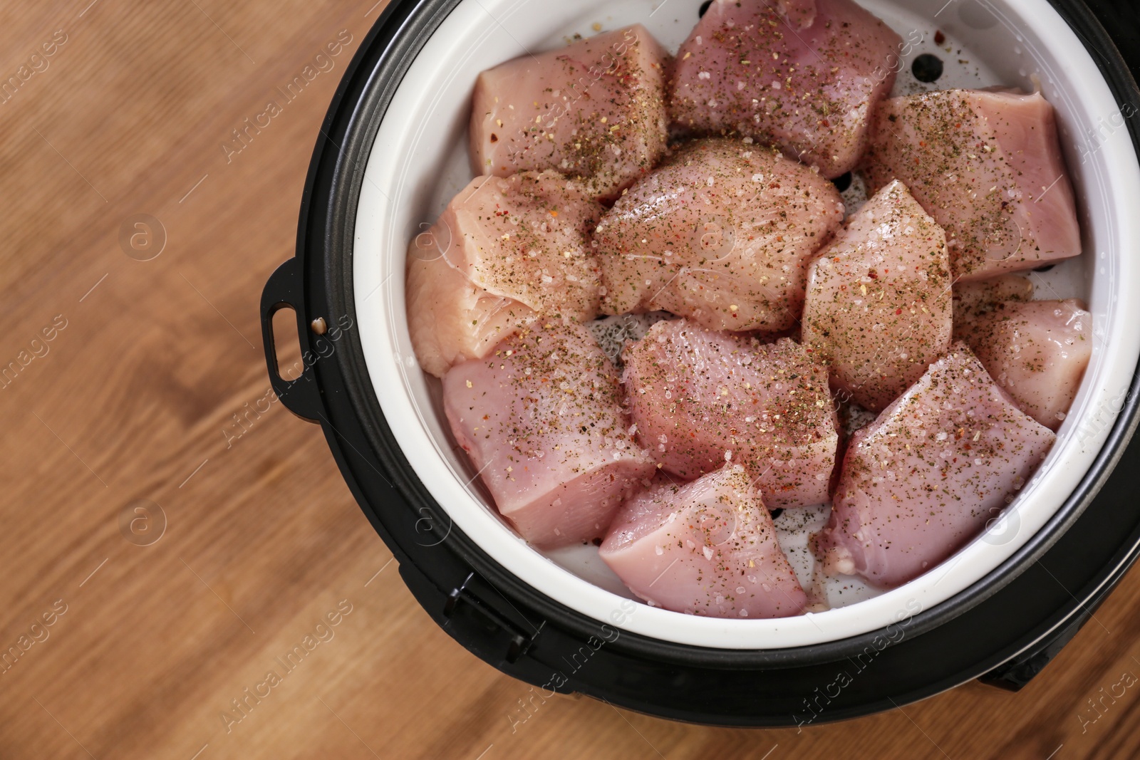 Photo of Delicious fresh chicken with spices in modern multi cooker on wooden table, top view. Space for text