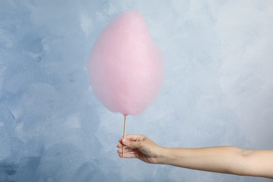 Photo of Woman holding sweet pink cotton candy on light blue background, closeup view