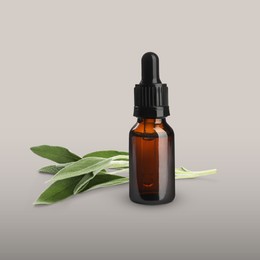 Image of Bottle of sage essential oil and green leaves on grey gradient background