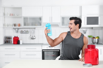 Young athletic man with protein shake powder in kitchen, space for text