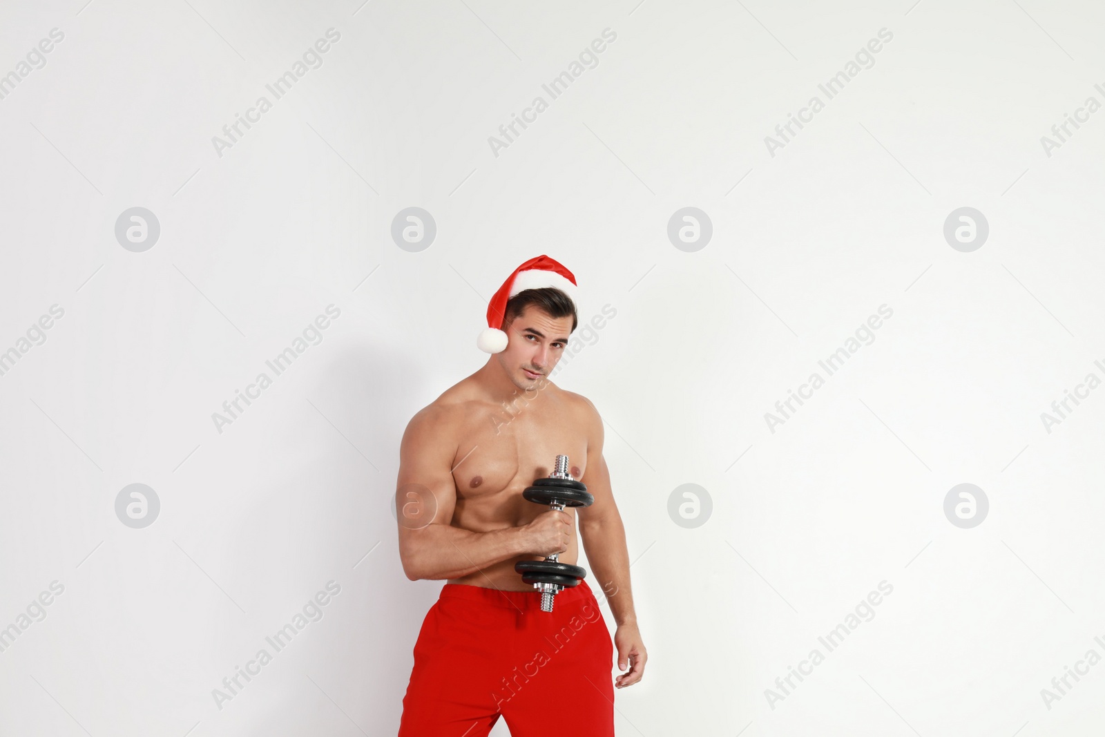 Photo of Sexy shirtless Santa Claus with dumbbell on light background
