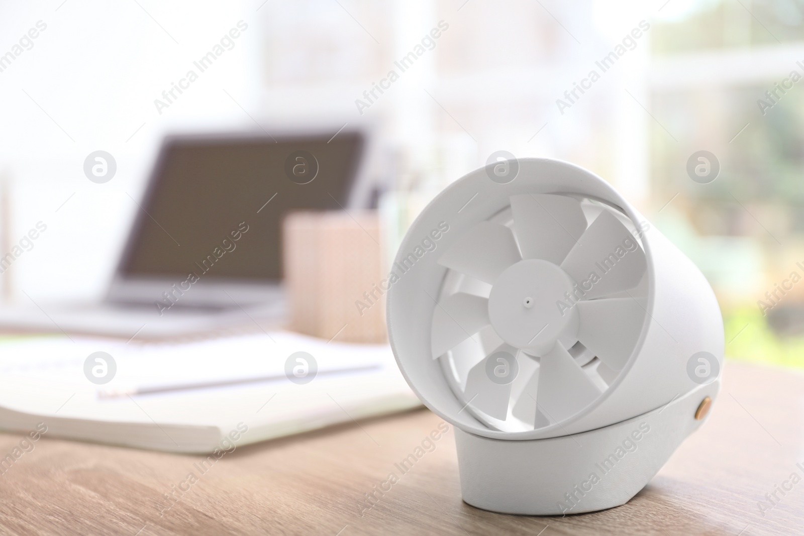 Photo of Modern portable fan on wooden table in office, space for text. Summer heat