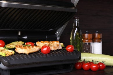 Photo of Electric grill with different products on wooden table