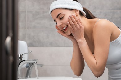 Young woman with headband washing her face in bathroom