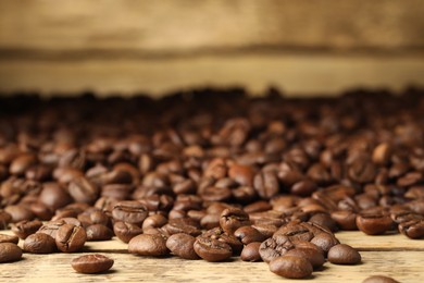 Many roasted coffee beans on wooden table, closeup
