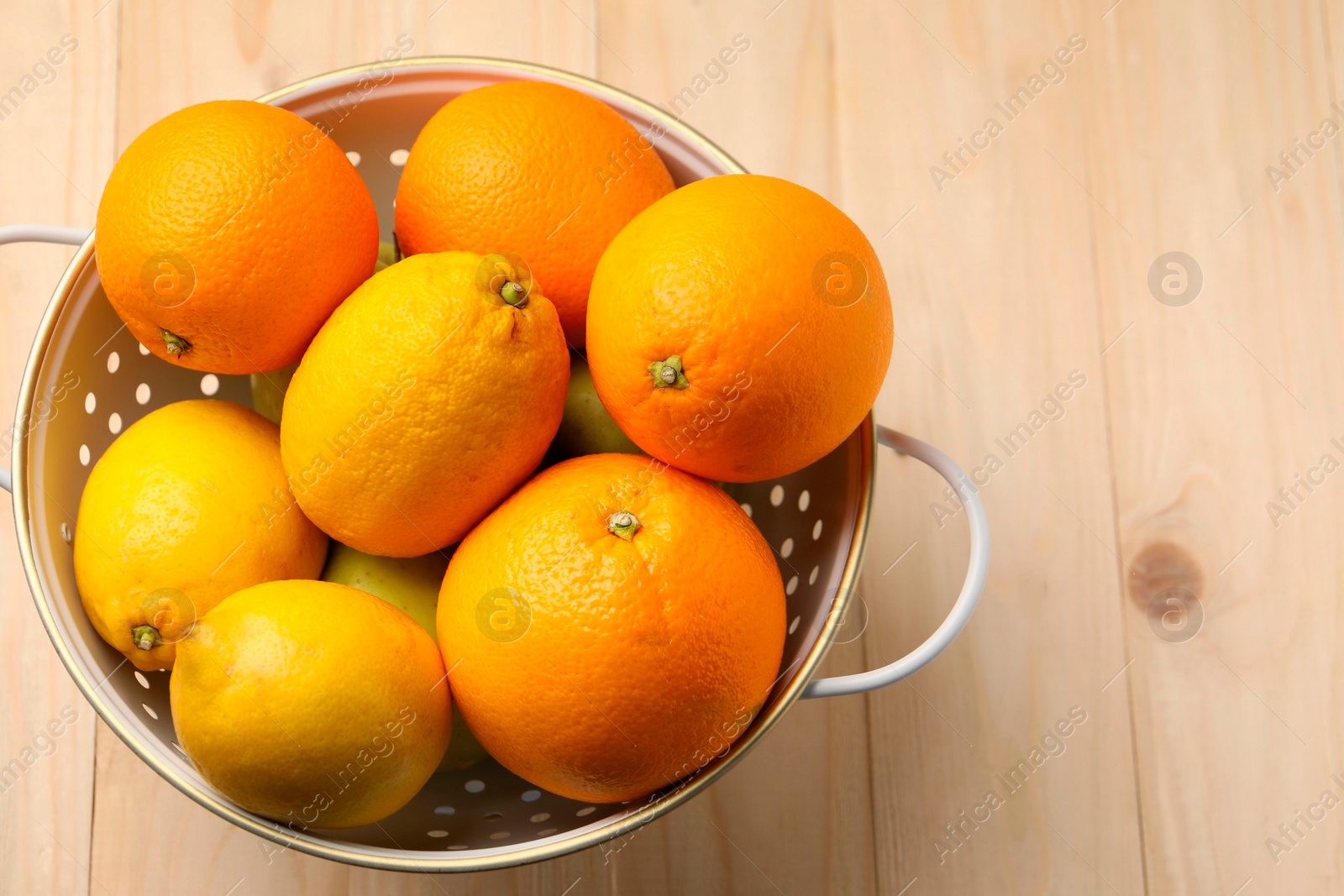 Photo of Colander with fresh citrus fruits on wooden table, top view. Space for text