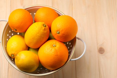 Colander with fresh citrus fruits on wooden table, top view. Space for text