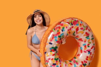 Photo of Young woman with straw hat holding inflatable ring against orange background