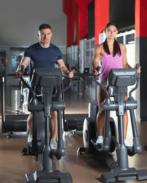 Couple working out on elliptical trainers in gym