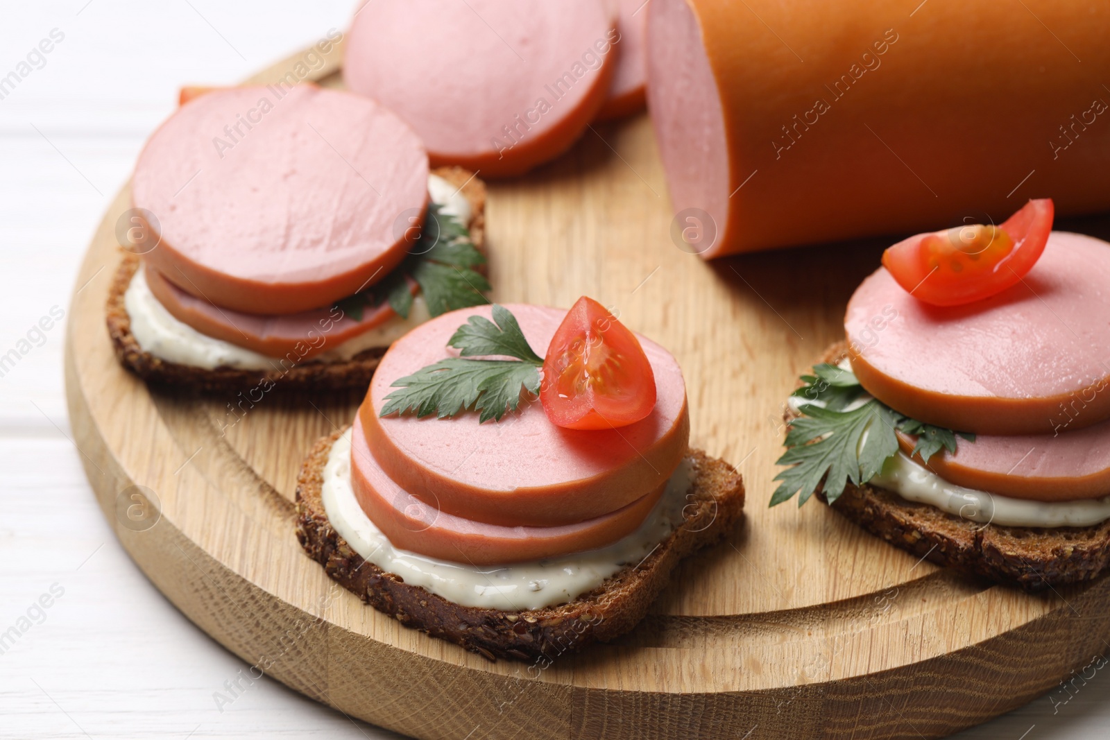 Photo of Delicious sandwiches with boiled sausage, tomato and sauce on white wooden table, closeup