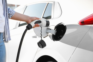 Photo of Woman inserting plug into electric car socket at charging station, closeup