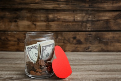 Photo of Donation jar with money and red heart on table. Space for text