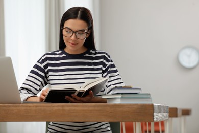 Young woman reading book at table in library
