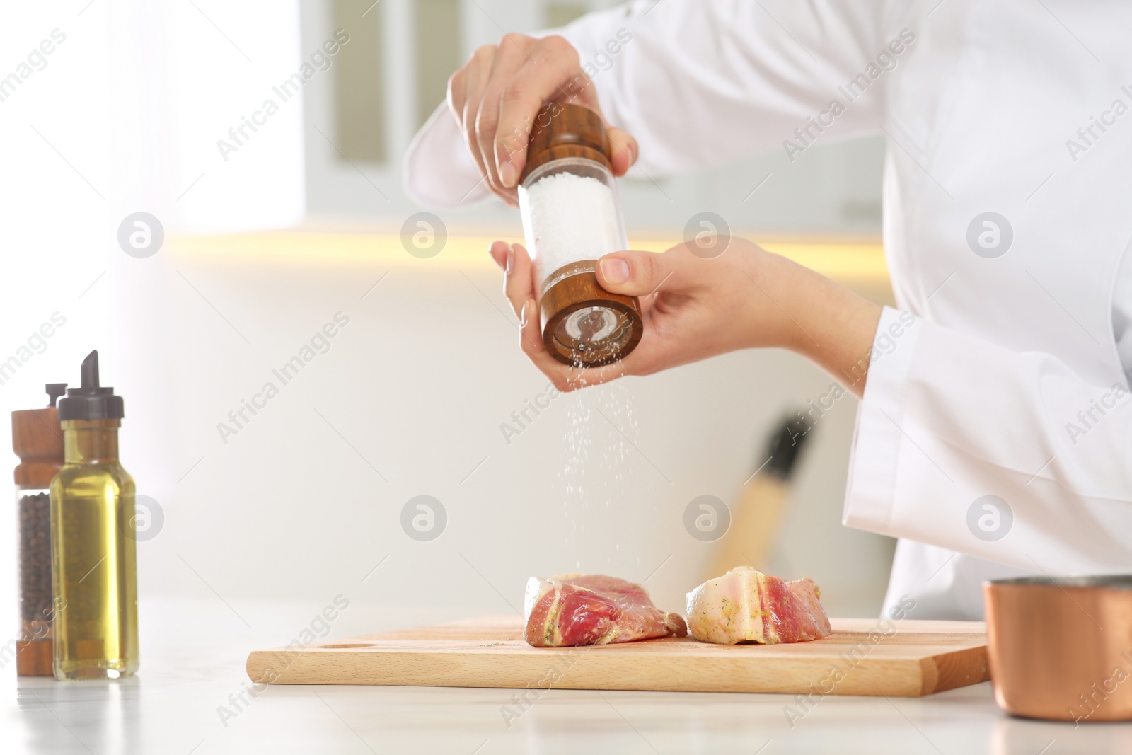 Photo of Professional chef adding pepper to delicious meat at white marble table, closeup