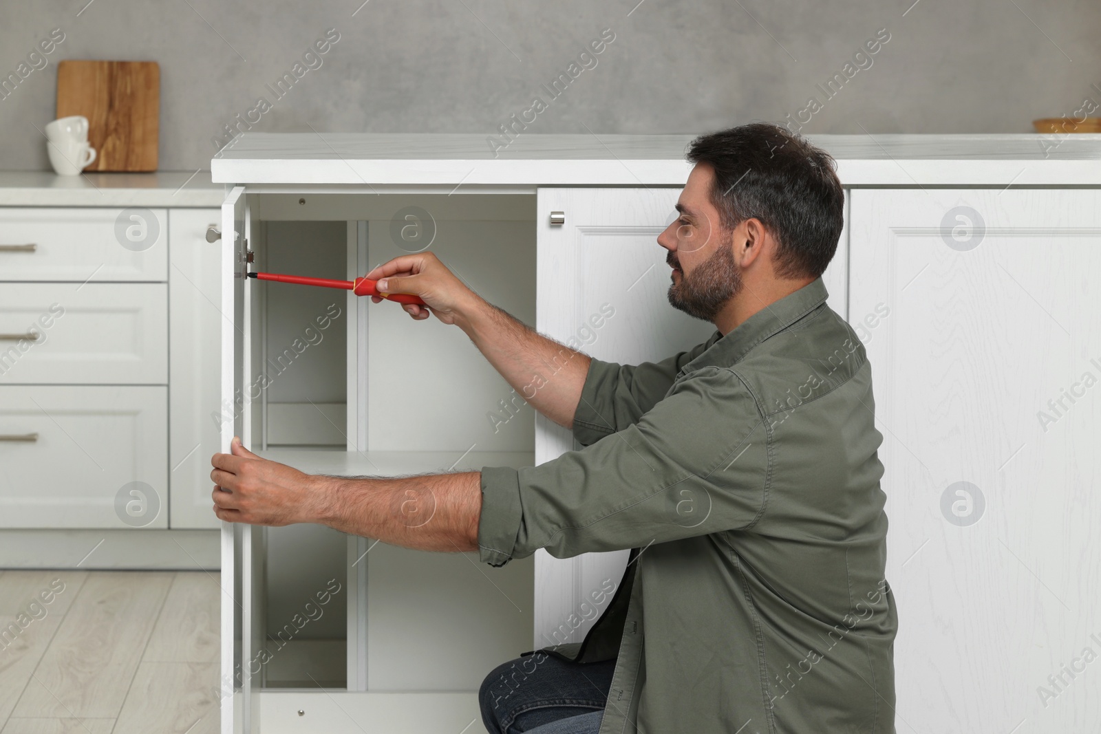 Photo of Man with screwdriver assembling furniture in kitchen