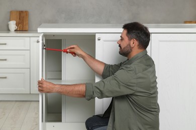 Man with screwdriver assembling furniture in kitchen