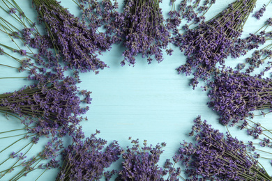 Frame with lavender flowers on light blue wooden table, flat lay. Space for text