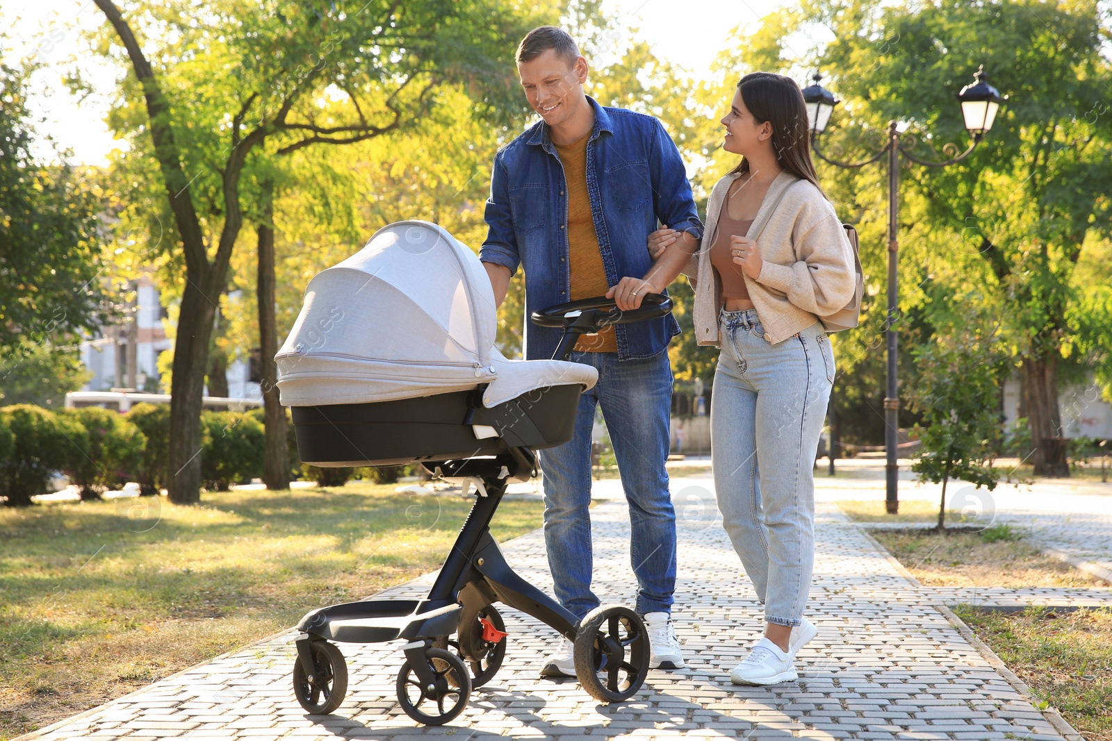 Photo of Happy parents walking with their baby in stroller at park on sunny day