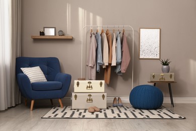 Photo of Stylish room interior with comfortable armchair, clothes and storage trunks