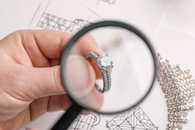 Jeweler examining diamond ring with magnifying glass at white table, closeup