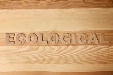 Photo of Word "Ecological" made of cardboard letters on wooden background, top view