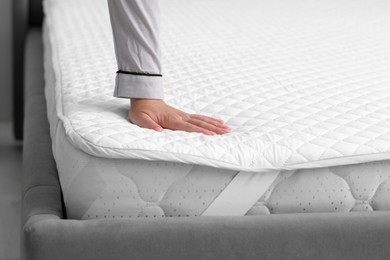 Photo of Woman touching new soft mattress on grey bed indoors. closeup