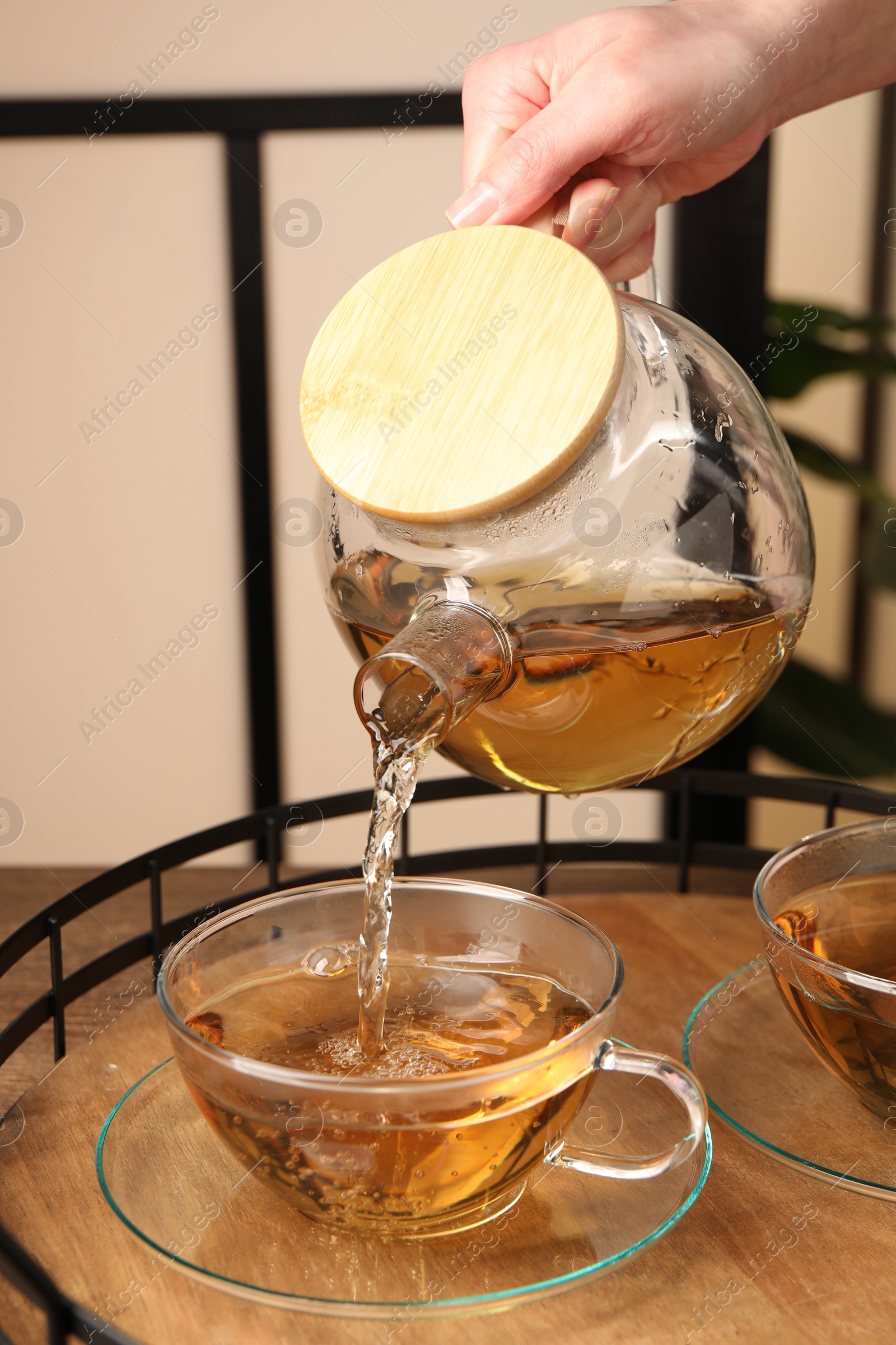 Photo of Woman pouring tasty tea into glass cup at table, closeup