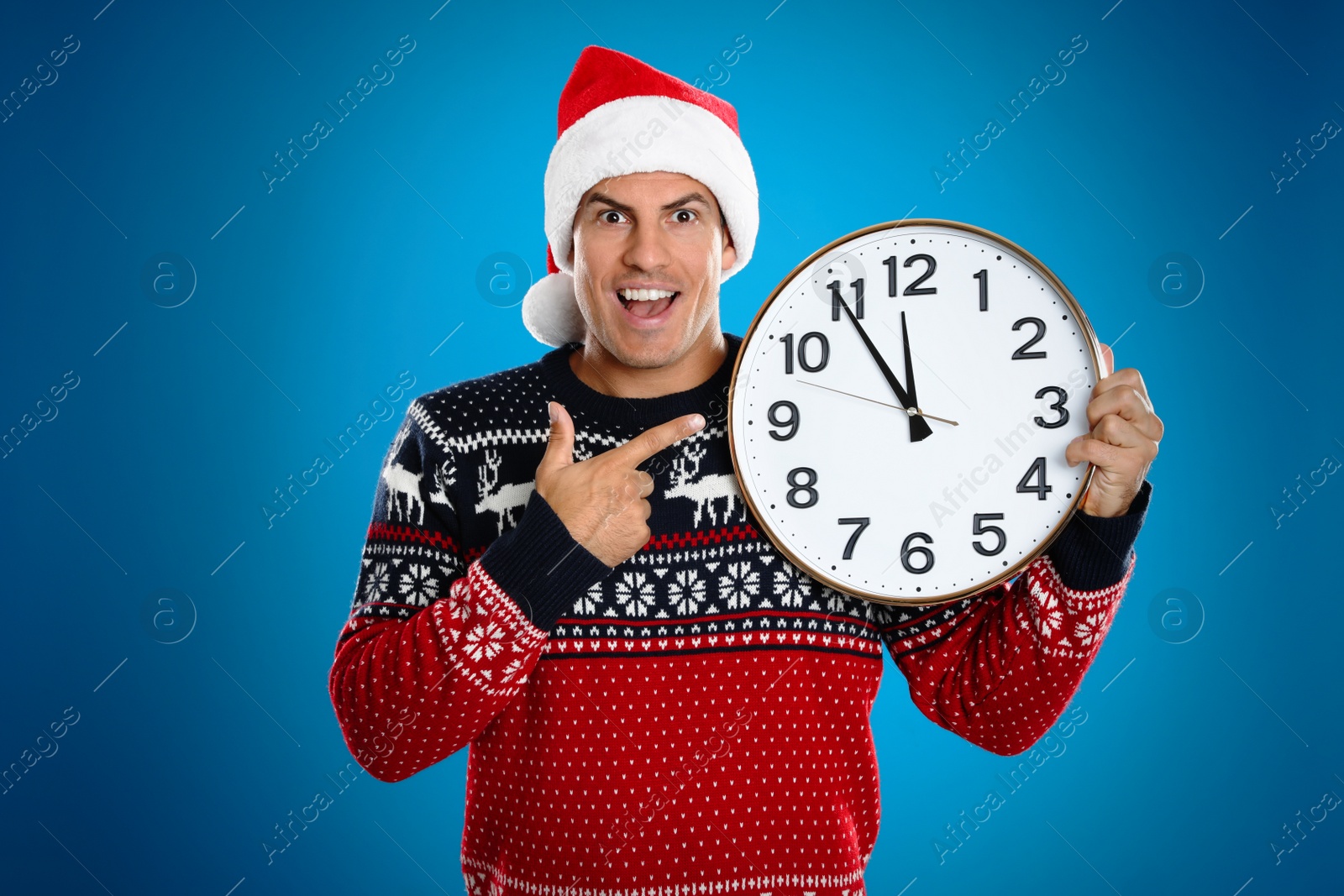 Photo of Man in Santa hat with clock on blue background. New Year countdown