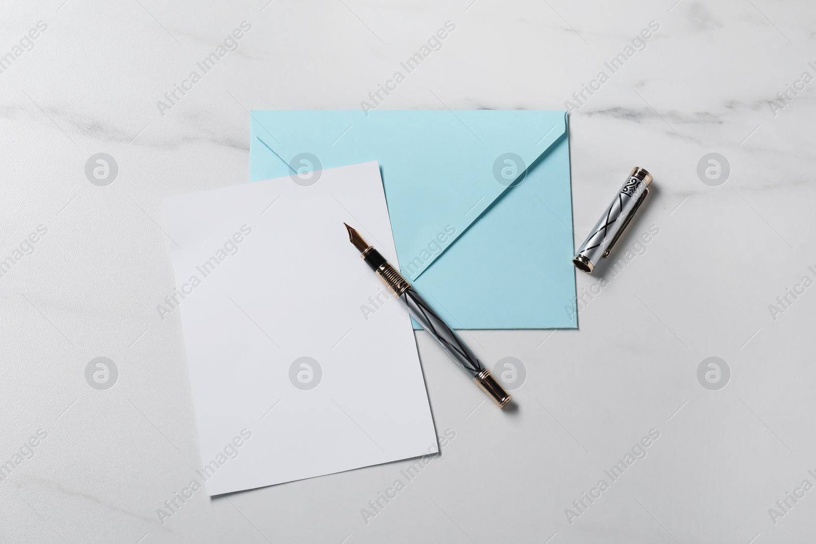 Photo of Blank sheet of paper, pen and letter envelope on white marble table, top view. Space for text