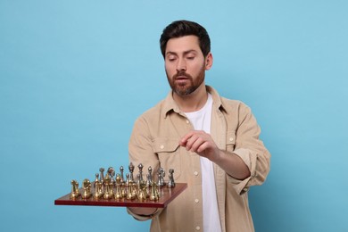 Photo of Handsome man holding chessboard with game pieces on light blue background