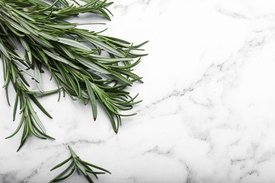 Photo of Sprigs of rosemary on white marble table, flat lay. Space for text