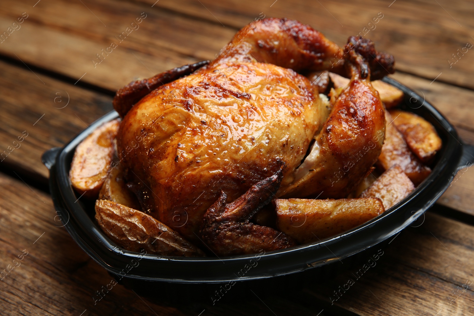 Photo of Delicious grilled chicken with potato in plastic container on wooden table. Food delivery service