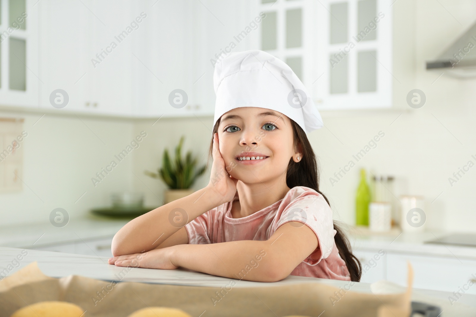 Photo of Cute little girl wearing chef hat in kitchen