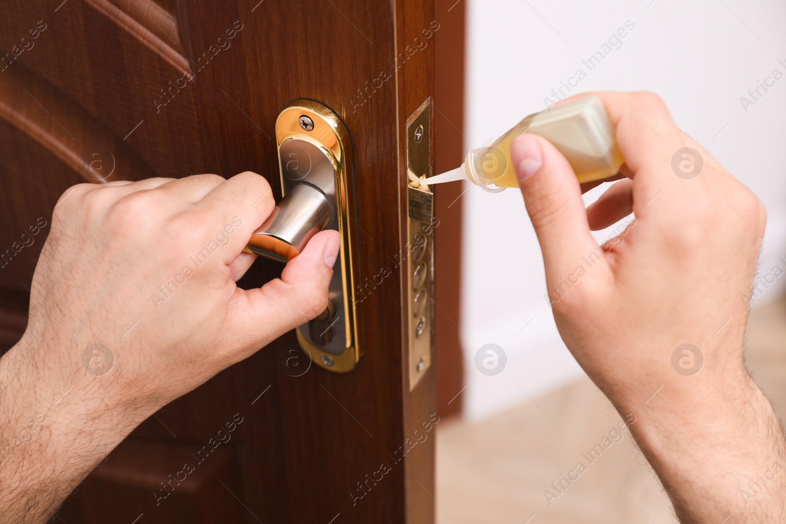 Photo of Repairman lubricating door lock indoors, closeup view