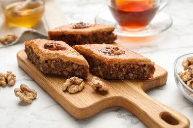 Photo of Delicious honey baklava with walnuts served on white marble table, closeup