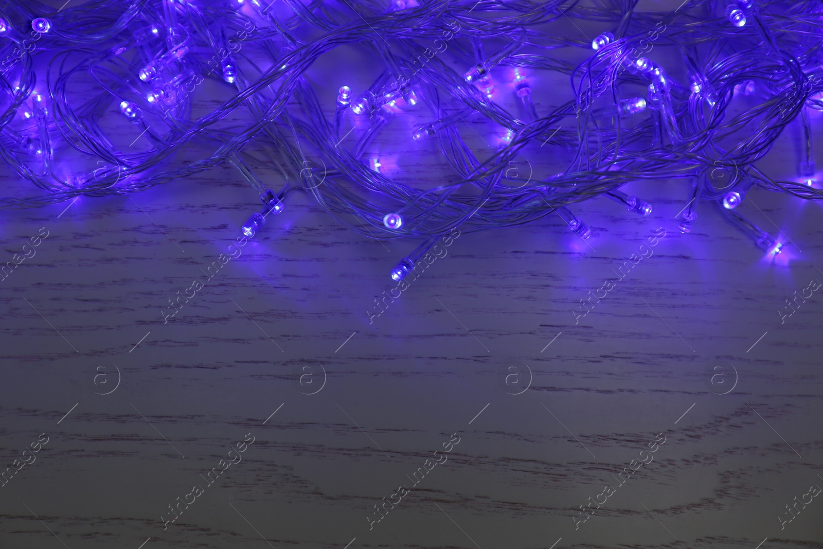 Photo of Blue Christmas lights on white wooden background, top view. Space for text