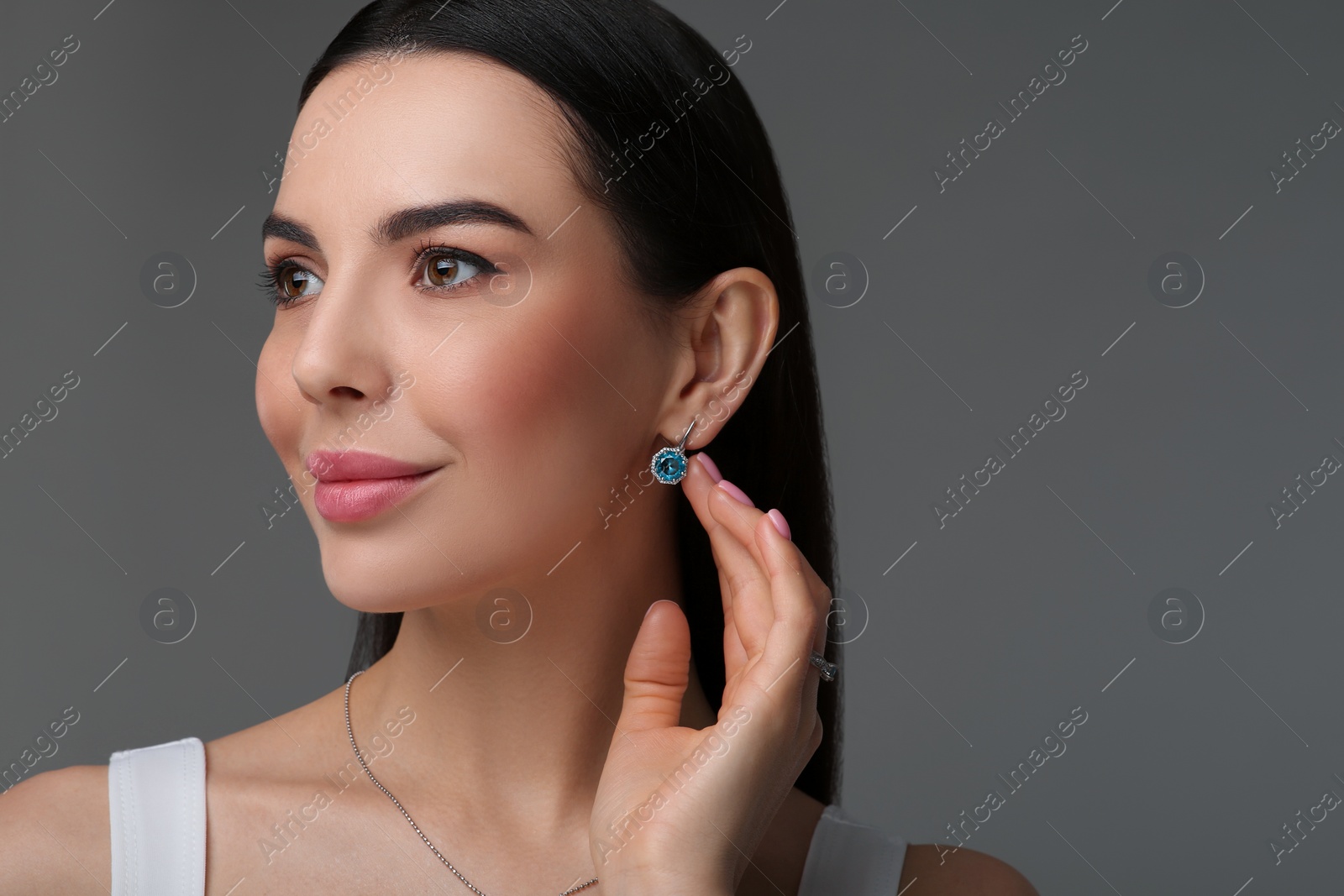 Photo of Beautiful young woman with elegant earrings on dark grey background