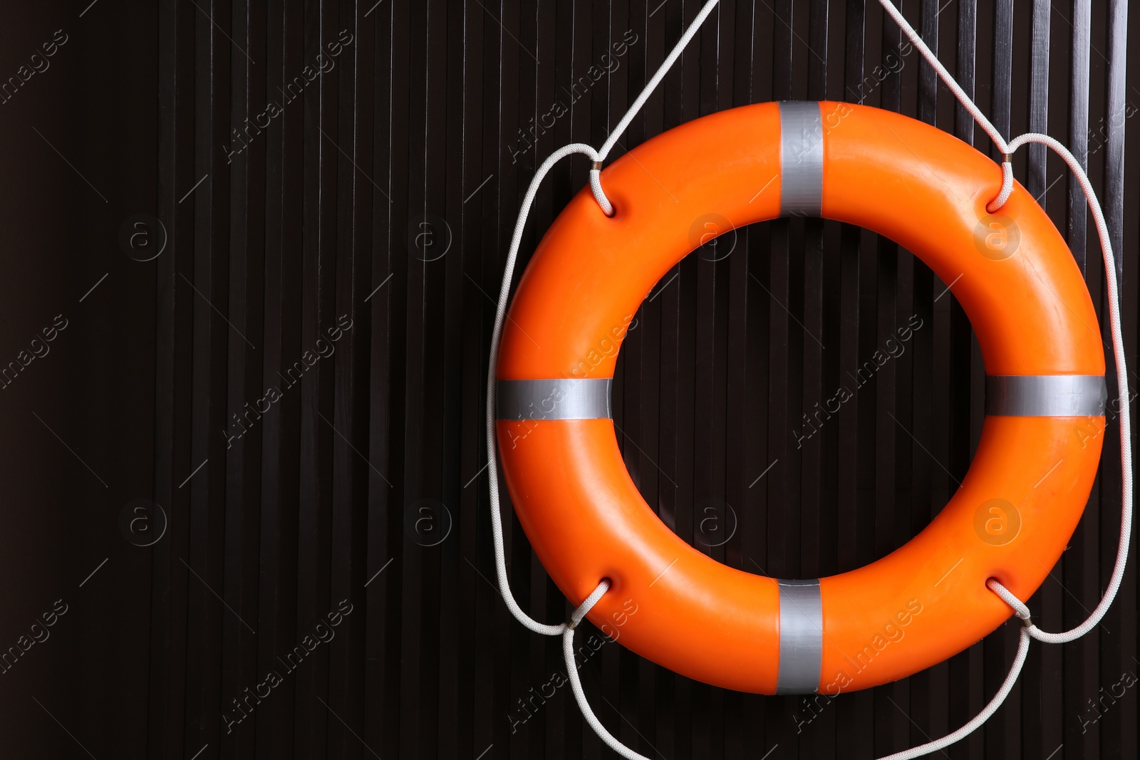Photo of Orange lifebuoy on dark wooden background, space for text. Rescue equipment