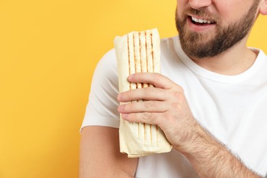 Photo of Young man with delicious shawarma on yellow background, closeup. Space for text
