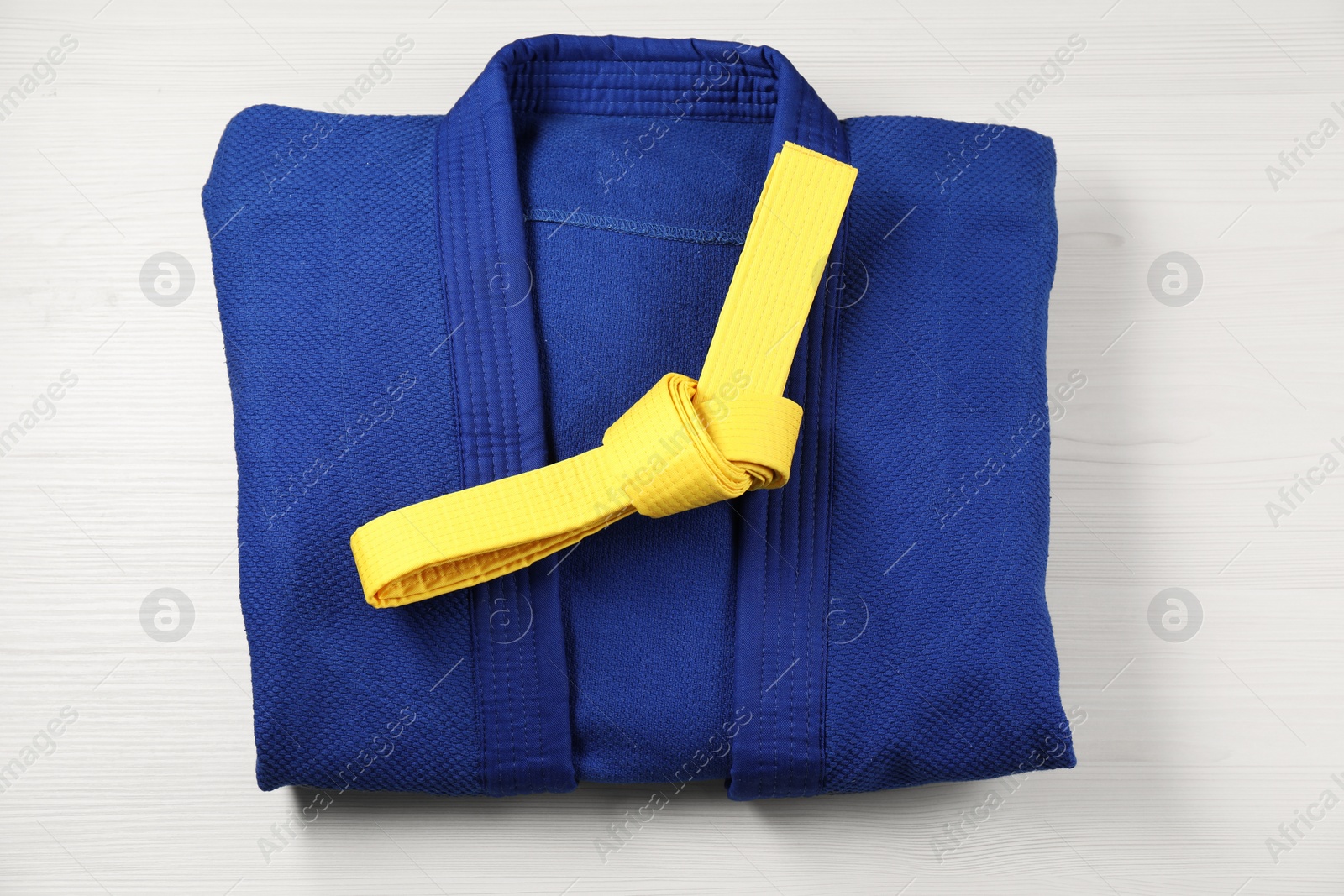 Photo of Yellow karate belt and blue kimono on wooden background, top view