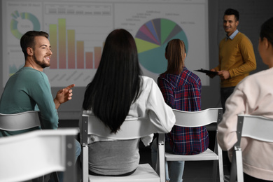 Photo of Young people having business training in conference room with projection screen