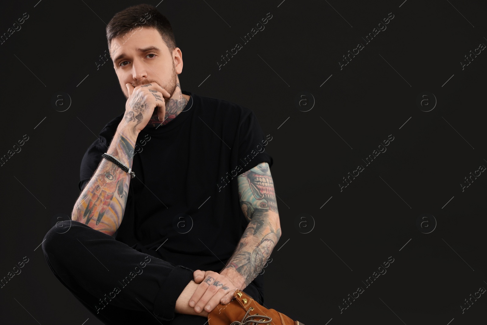 Photo of Handsome hipster man posing on chair against black background. Space for text