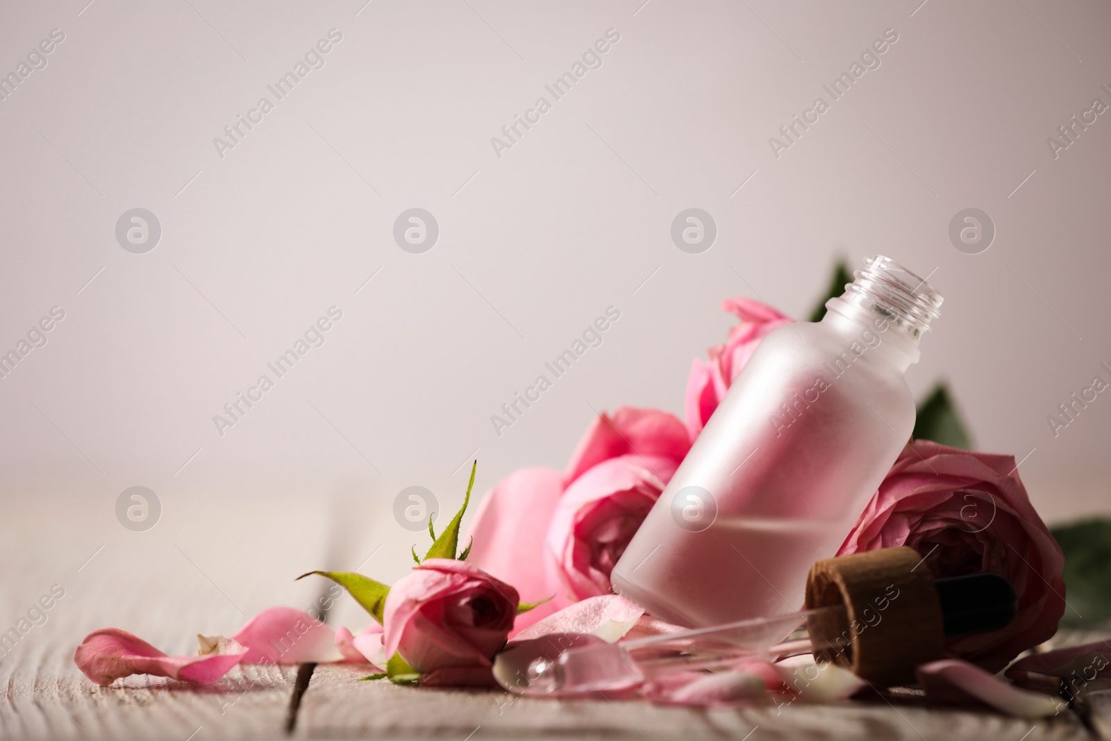Photo of Bottle of essential oil and roses on white wooden table against light background. Space for text