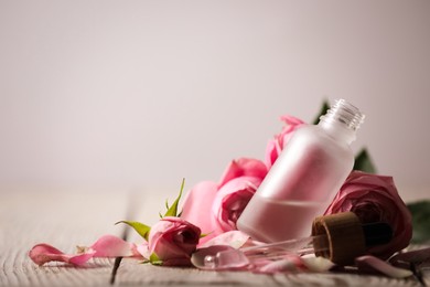 Photo of Bottle of essential oil and roses on white wooden table against light background. Space for text