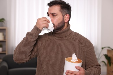 Photo of Sick man with tissue blowing nose at home. Cold symptoms