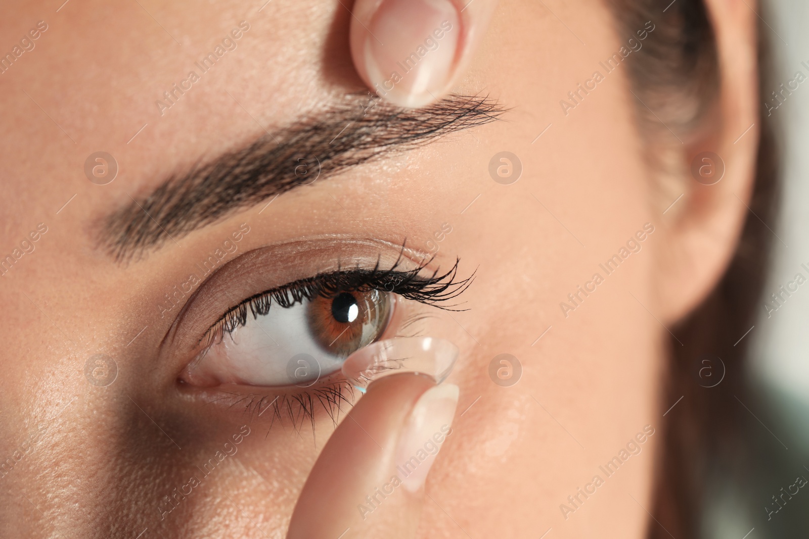 Photo of Young woman putting contact lens in her eye, closeup